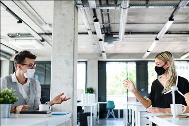 two employees practicing social distancing and working staggered shifts in a flexible work environment