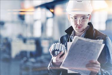 quality control professional examining piece of equipment and spec sheet