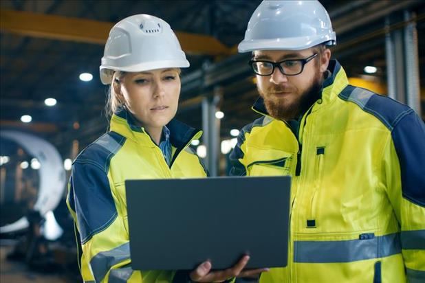 two manufacturing employees in a factory reviewing information on a laptop