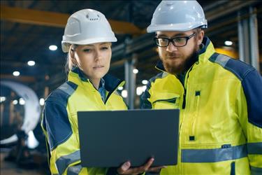 two manufacturing employees in a factory reviewing information on a laptop