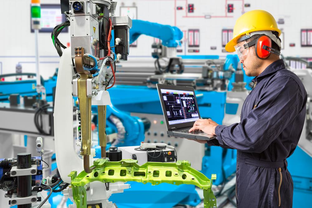 manufacturing employee using a laptop while examining an equipment system