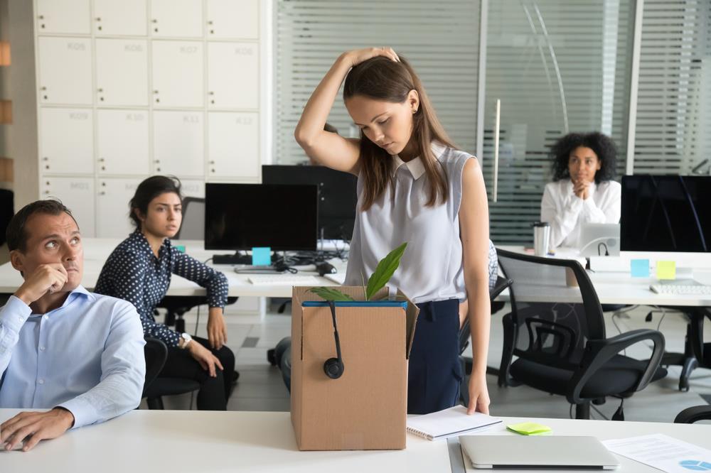 Upset employees watching laid-off colleague pack up desk