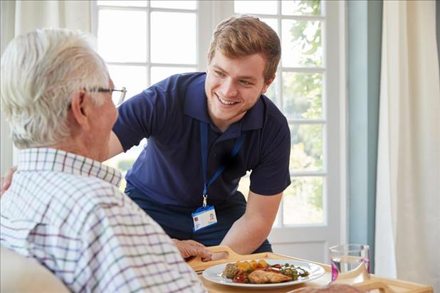 male home health aide helping a patient enjoy his meal