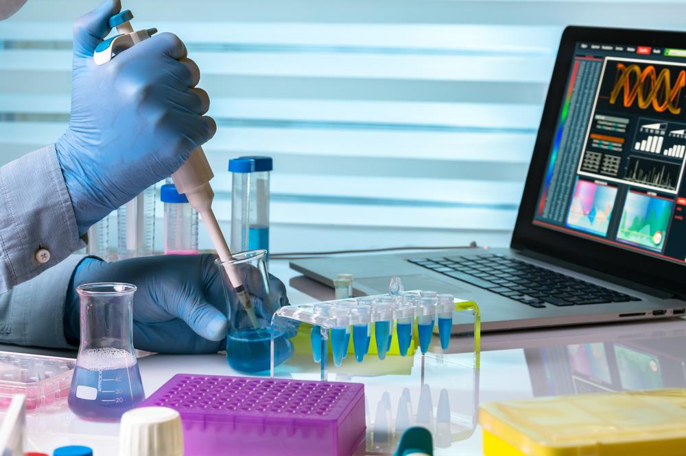 analytical chemist working on samples in the lab while looking at data on a laptop