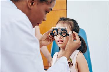 optometry professional performing an eye exam on a girl