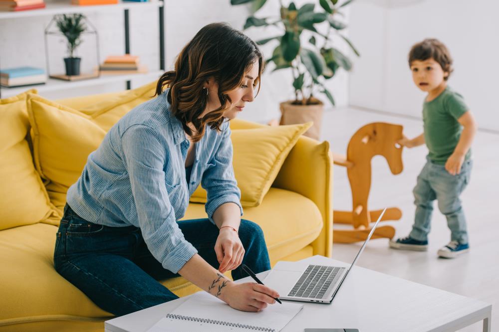 Woman working from home while her child plays in the background