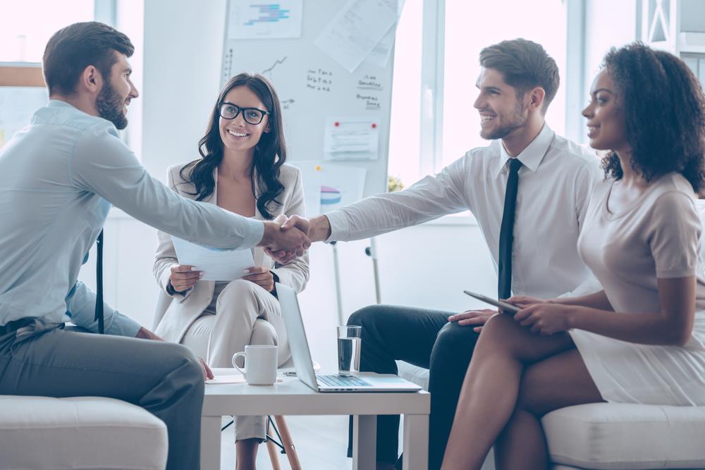 interviewee shaking the hand of an interviewer with colleagues smiling in the background