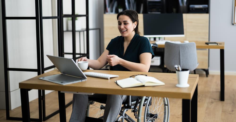 employee in a wheelchair smiling while meeting virtually at her desk