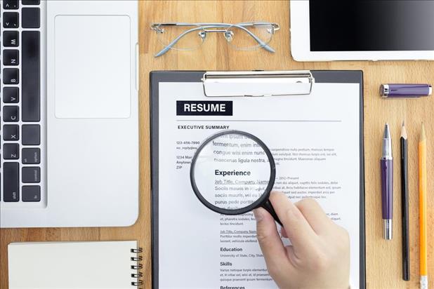 HR Manager reviewing a resume on his desk with Magnifier, computer laptop, digital tablet, calculator and glasses.