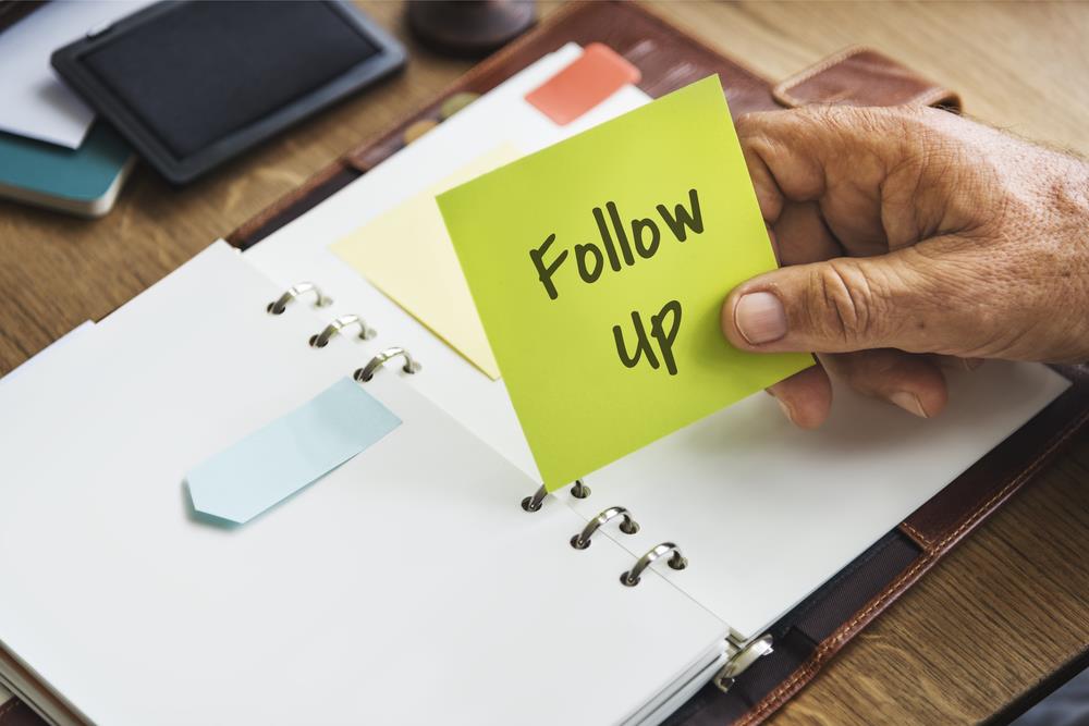 Person holding up a post-it note that reads follow up