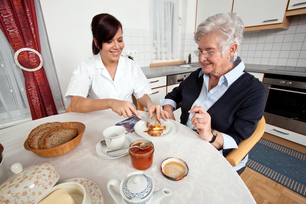 caregiving professional helping an elderly patient with breakfast in her home