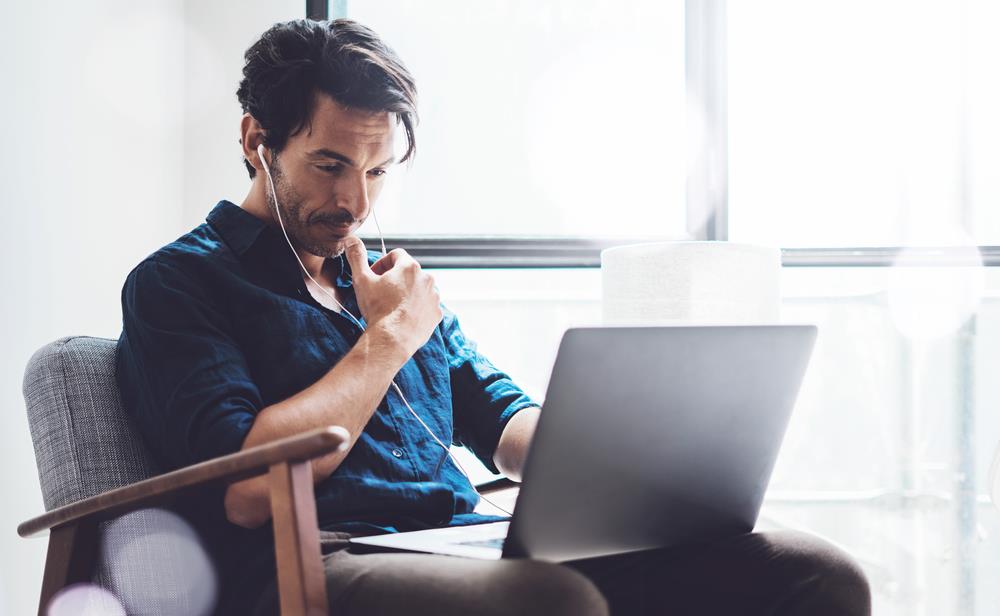 Professional wearing headphones and thinking while looking at laptop