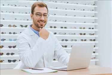 an optometrist writing an optician job ad on his laptop