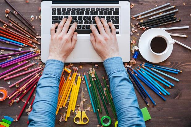 graphic designer working on their laptop with colored pencils all around