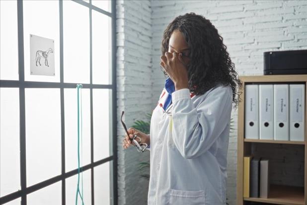 veterinarian rubbing her eyes tiredly in her office