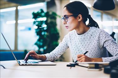 Woman researching on laptop and taking notes